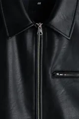 Campera de cuero sintético color negro con cuello camisero, cierre frontal, bolsillo superior con cierre y bolsillos laterales ribeteados.