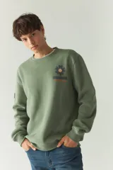 Buzo de felpa verde oliva con cuello redondo y puños y bajo acanalados. Estampado con una flor y la marca Mustang en el pecho.