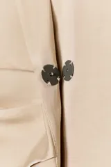 Blazer color beige claro, de corte cruzado con solapa con muescas, hombreras y manga larga. Presenta un detalle de pliegues drapeados en el delantero.