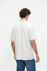 Remera polo manga corta color blanco, confeccionada en tela piqué de algodón lavado con textura extra suave. Cuenta con media cartera de botones, cuello y puños acanalados con diseño de líneas a contratono, y bordado sutil de la marca en el pecho. Calce clásico.