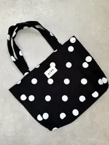 Tote bag de algodón color negro con estampado de lunares blancos. Cuenta con doble asa de hombro y etiqueta frontal con el logo de la marca.