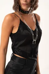 Top de satén negro con escote en V, decorado con detalles de encaje floral en el escote y en el ruedo. Presenta breteles finos ajustables y un corte asimétrico en la parte inferior.