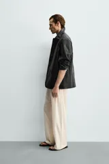 Sobrecamisa de corte relaxed fit confeccionada en tejido efecto piel de color negro, con cuello solapa, manga larga, bolsillos con solapa en la cadera y cierre frontal de botonadura.