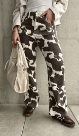 Pantalón de jean de corte recto con estampado de manchas de vaca en tonos marrón y blanco.