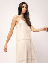 Vestido largo color crudo de lino, con silueta recta, escote en V, breteles anchos, detalle de elástico en la espalda y tajos laterales.