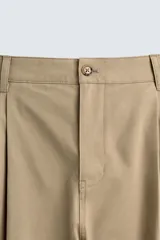 Pantalón chino de corte wide fit confeccionado en tejido de algodón. Presenta pliegues frontales, bolsillos laterales y bolsillos traseros de vivo, con cierre frontal de cremallera y botón.