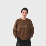 Sweater de punto acanalado en color marrón, con cuello redondo y logo bordado en el pecho. Presenta un diseño de corte holgado con mangas largas.