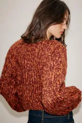 Jersey de punto grueso con textura trenzada en color naranja y bordó. Presenta cuello redondo, mangas largas abullonadas y detalle de cordones trenzados a contraste en el frente con terminación en lazada en el ruedo.