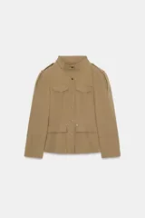 Blazer entallada color beige con cuello subido, manga larga con hombreras y trabillas en los hombros. Presenta bolsillos de plastrón en el delantero, detalle de solapas en el pecho y cierre frontal con botones a presión.