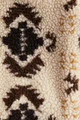 Buzo oversized de sherpa suave en color beige con estampado geométrico en tonos marrones y detalles en tejido revestido. Presenta cuello elevado, medio cierre frontal y bolsillos laterales.