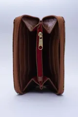 Billetera marrón tipo sobre con cierre de cremallera, confeccionada en cuero con textura tipo cocodrilo y forro textil rojo. Cuenta con múltiples ranuras para tarjetas, documentos y billetes.