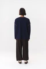 Remera de manga larga con corte oversized, color azul marino con cuello redondo en contraste color marrón. Presenta costuras decorativas a contratono hechas a mano en la zona de los hombros y logo bordado en el centro del pecho.