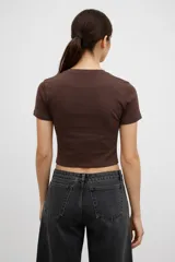 Remera de algodón color marrón, de corte crop y ajuste al cuerpo, con cuello redondo y aplique central en forma de corazón con estampado a cuadros.