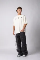 Remera de corte oversize color negro, confeccionada en algodón premium. Presenta un diseño gráfico minimalista estampado en el frente con tipografía y logotipos en color crema.