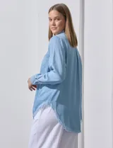 Camisa celeste de tencel, marca Hester & Orchand. Tiene cuello con solapa, escote en V, abertura central con botones, bolsillo aplicado en el frente y ruedo desflecado.