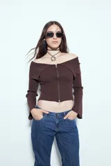 Top de punto acanalado negro, con diseño off-shoulder y escote amplio. Presenta mangas largas y cierre frontal completo con doble cursor, permitiendo ajustar la apertura superior e inferior.
