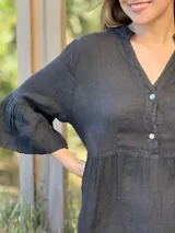 Vestido corto de lino color beige claro, con cuello mao, escote con botones de nácar, mangas tres cuartos con volados y ruedo con volado.