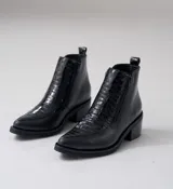 Bota corta de cuero vacuno color negro, con diseño combinado de cuero liso y cuero con textura de reptil en el empeine. Presenta punta fina, taco cuadrado de 6 cm y doble cierre lateral.
