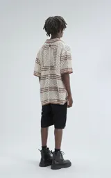 Camisa de manga corta tejida en punto abierto (símil crochet), color beige con detalles en marrón. Presenta cuello solapa, cierre frontal con botones y calce oversize.