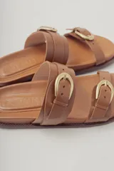 Sandalias planas de cuero negro con diseño de dos tiras ajustables con hebillas metálicas.