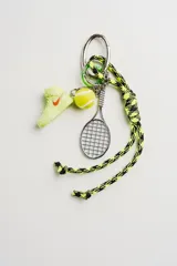 Llavero deportivo con cordón trenzado en color amarillo neón y negro. Incluye tres dijes colgantes: una zapatilla tipo sneaker color verde lima con logo naranja, una pelota de tenis y una raqueta de tenis de metal plateado.