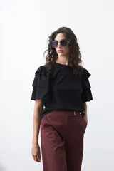 Remera negra de algodón con cuello redondo y mangas cortas con volados en capas que aportan volumen y movimiento.