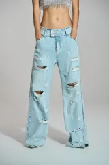 Jean wide leg de mujer en denim azul claro, con efecto desgastado, aberturas y aplicaciones de pedrería brillante distribuidas a lo largo de la silueta.