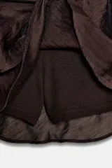 Falda pantalón de tiro medio color marrón oscuro, con frunces laterales y volantes en el bajo. Incluye un cinturón ancho decorado con círculos metálicos y remaches dorados.