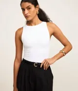 Body blanco de poliamida con cuello halter, sin mangas y sin estampado. Tiene forro en el busto y un corte que modela el cuerpo.