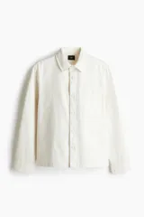 Sobrecamisa color crema de sarga de algodón, corte regular, con cuello inglés, tapeta clásica, bolsillo de parche en el pecho, mangas largas con puños abotonados y bajo recto.