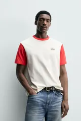 Remera de corte regular fit en color blanco con cuello redondo y mangas cortas en color rojo contrastante, y aplicación de parche bordado en el pecho.