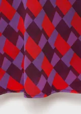 Blusa sin mangas con cuello drapeado, confeccionada en tejido fluido con estampado geométrico en tonos rojos y violetas.