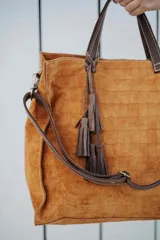 Bolso tipo tote de cuero gamuzado en color marrón, con textura grabada tipo cocodrilo, manijas de cuero oscuro y detalle de borla colgante.