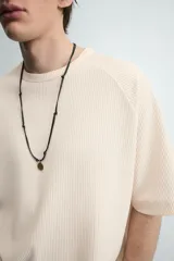 Camiseta de manga corta color crema, con cuello redondo y tejido acanalado verticalmente, de corte holgado (boxy fit).