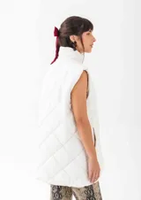 Chaleco acolchado de corte recto y largo medio, con diseño de rombos, cuello alto y cierre frontal con botones a presión.