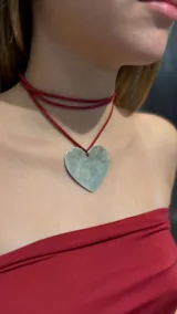 Gargantilla tipo choker compuesta por un cordón de gamuza roja que se envuelve alrededor del cuello, con un dije grande en forma de corazón de metal con acabado envejecido.