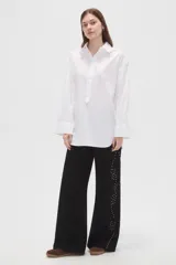 Camisa blanca de algodón, de corte holgado, manga larga con puños anchos y cuello camisero. Cuenta con cierre frontal parcial de botones.