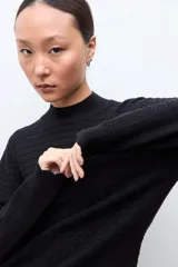 Sweater de punto color crudo con cuello alto tipo media polera, manga larga y diseño con textura de líneas horizontales. Presenta un borde inferior con terminación ondulada.