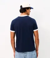 Remera masculina de corte regular, confeccionada en algodón negro, con cuello redondo y mangas cortas con puños blancos. Presenta tiras laterales con rayas en los hombros y mangas.