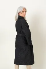 Trench negro capitoneado con bordado floral, corte clásico, cuello solapa, cierre cruzado con broches, lazo para ajustar en la cintura y bolsillos laterales.