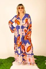 Vestido largo azul con estampado de flores en tonos naranja, rosa y marrón. Tiene cuello en V, mangas largas acampanadas y corte escalonado con volantes.
