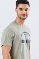 Remera verde pistacho de manga corta y cuello redondo, con diseño gráfico estampado en el frente con inscripciones y tipografías en tonos oscuros y blancos.