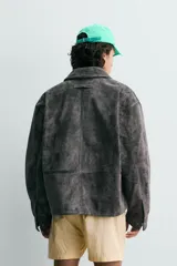 Cazadora de corte relajado confeccionada en piel con acabado de serraje. Presenta cuello solapa, cierre frontal con cremallera oculta bajo solapa con botones a presión, bolsillo con cremallera en el pecho y bolsillos de plastrón con solapa en la cadera. Incluye efecto vintage en las costuras y puños con botón.