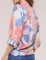 Blusa estampada Zac & Rachel con diseño floral en tonos rosados, azules y amarillos sobre base blanca. Presenta escote en V con botones frontales, mangas tres cuartos con presilla para arremangar y detalle de nudo en el ruedo.