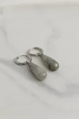 Aros tipo argolla de acero quirúrgico con dije colgante en forma de gota de piedra natural en tono marrón.