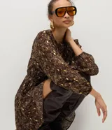 Vestido corto de chiffon con estampado paisley en tonos marrones y detalles metalizados dorados. Presenta mangas largas con puños elásticos, cuello redondo y falda con caída fluida.