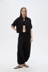 Camisa negra de viscosa, holgada, con mangas cortas abotonadas, cuello camisero, detalles de cintas decorativas verticales y cierre frontal con botones.
