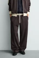 Pantalón jogger de corte wide fit en tejido compacto color gris oscuro. Presenta cintura elástica con cordón ajustable, bandas laterales en contraste color beige y costuras frontales tipo pinza.