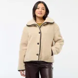 Campera de efecto borreguito en color beige, con cuello amplio y cierre frontal de botones negros. Presenta ribetes negros en contraste en el cuello, la apertura frontal y los puños. Marca Kiabi.