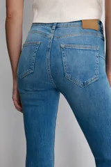 Jeans de tiro medio con corte bootcut y ajuste slim. Presenta diseño de cinco bolsillos, trabillas en la cintura y cierre frontal con cremallera y botón. Incluye detalle de pespuntes marcados a contraste.